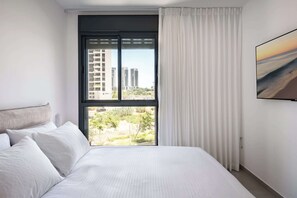 Een hotelkamer met een groot raam, een bed en uitzicht op gebouwen en groen.