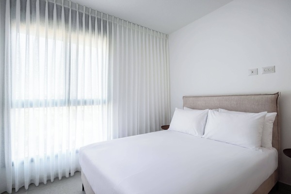 Serene bedroom with expansive sheer curtains, natural window light, beige headboard, and tranquil minimalist atmosphere.