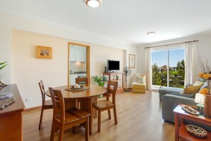 A dining area with a wooden table and chairs, a kitchen with cabinets, a TV, and a balcony with a view. - Apartment 'Ajuda Mar Holidays with Parking' with Balcony and Wi-Fi (Funchal)