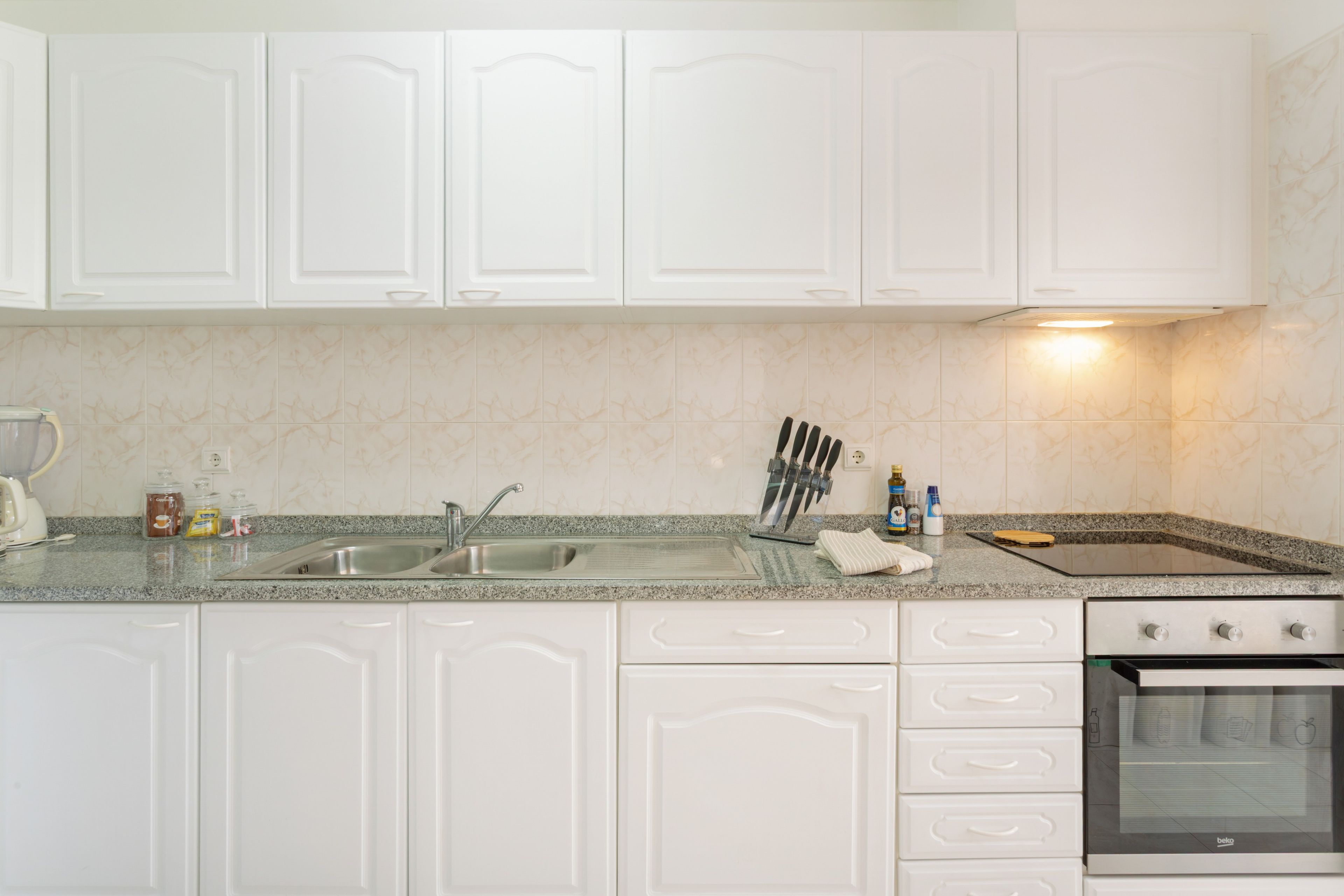 A kitchen with white cabinets, a granite countertop, a sink, and a stove.