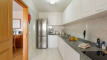 A modern kitchen with white cabinets, a stainless steel refrigerator, a granite countertop, and a dining area with a wooden table and chairs.