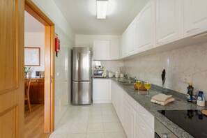 A modern kitchen with white cabinets, a stainless steel refrigerator, a granite countertop, and a dining area with a wooden table and chairs. - Apartment 'Ajuda Mar Holidays with Parking' with Balcony and Wi-Fi (Funchal)