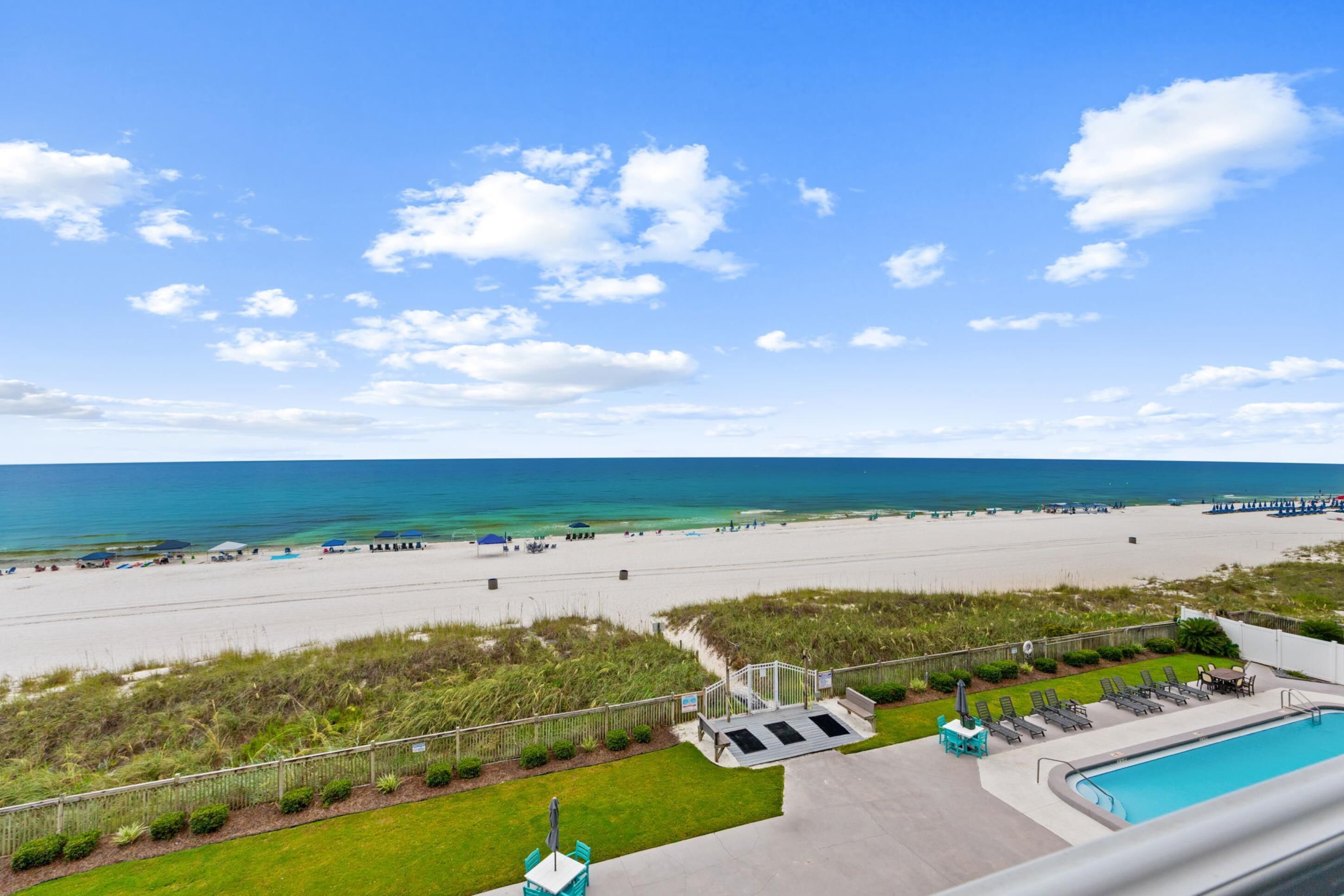 A beach view with a swimming pool, lounge chairs, and a staircase leading to a grassy area.