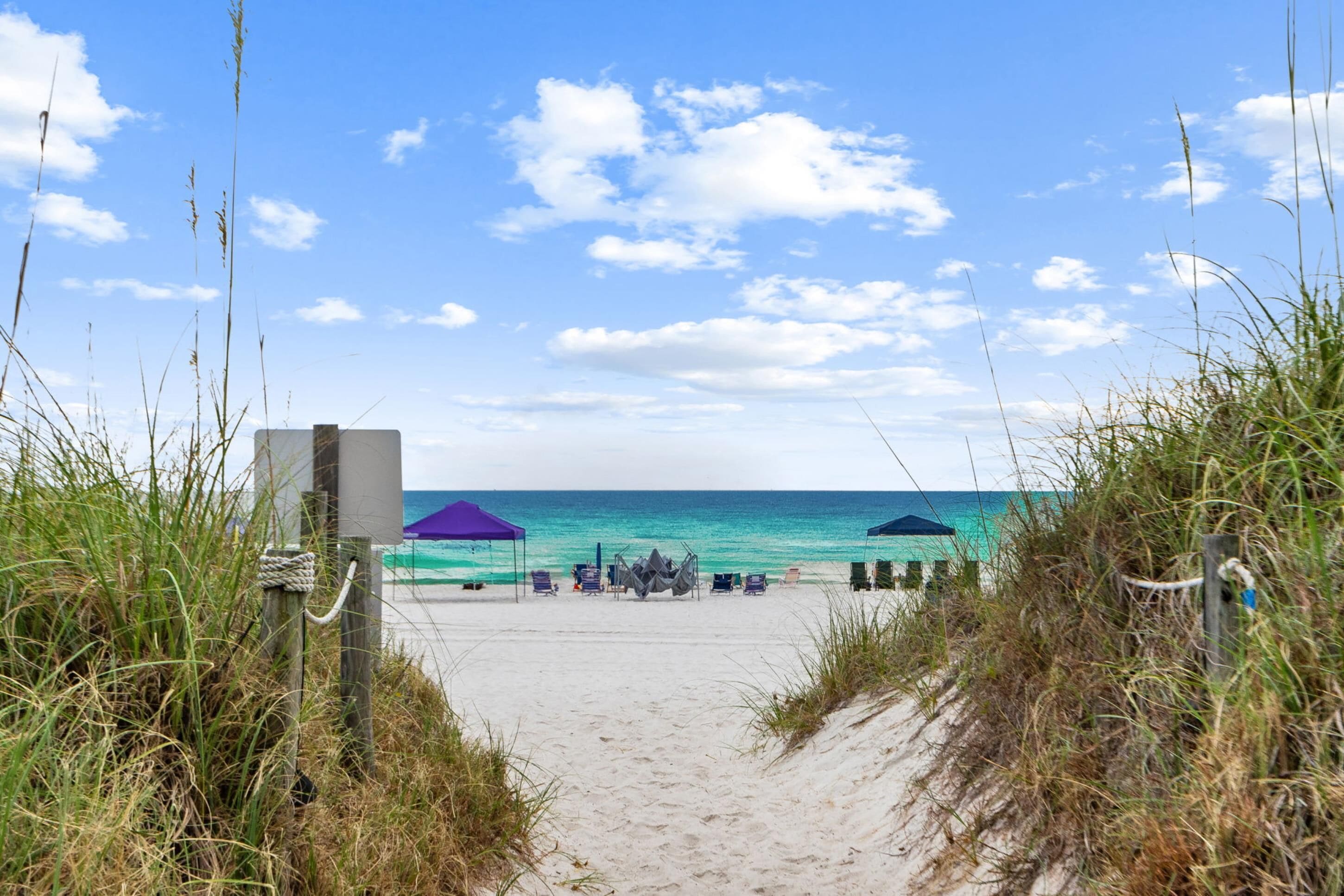 A beach path leading to a sandy beach with umbrellas and lounge chairs.
