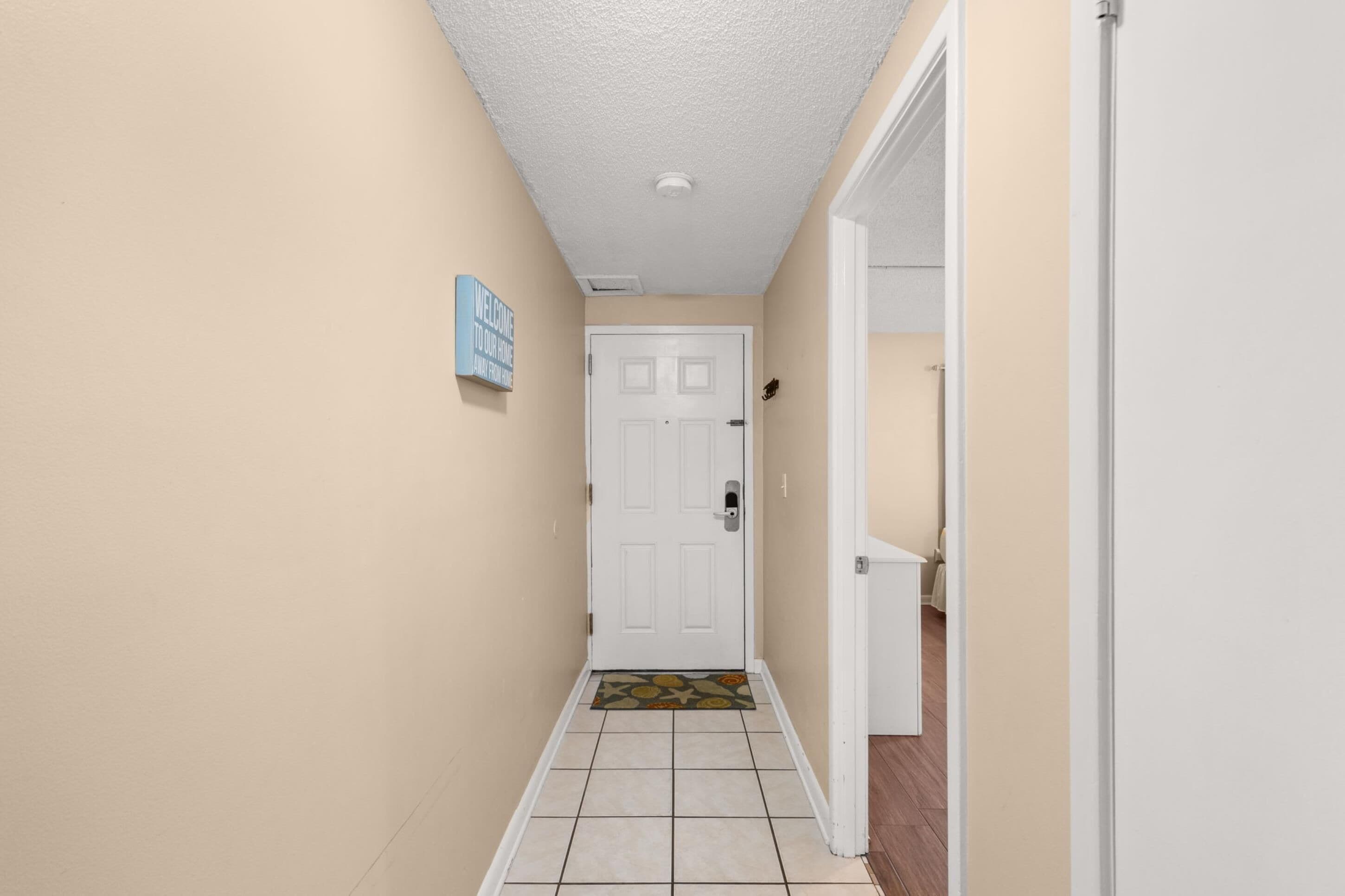 A hallway with a white door, beige walls, and a welcome sign.