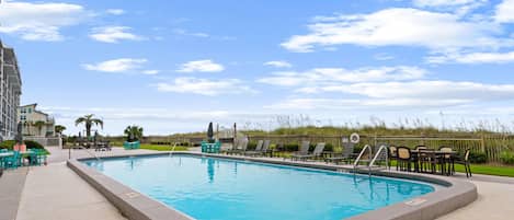 A swimming pool with lounge chairs and tables, surrounded by a fence and a grassy area.