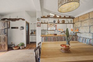 Eine rustikale Küche mit einem Holztisch, einer hängenden Leuchte und einer Steinwand.