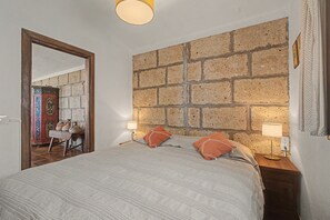 Ein Schlafzimmer mit einem großen Bett, zwei Nachttischlampen, einer Steinwand und einer Holztür.