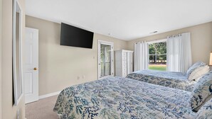 Ein Schlafzimmer mit zwei Betten, einem an der Wand befestigten Fernseher, einer Tür und einem Fenster mit Vorhängen.