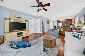 Ein Wohnzimmer mit Fernseher, Sofas, Couchtisch und Deckenventilator.