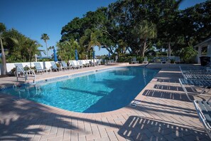 A swimming pool with lounge chairs and umbrellas, surrounded by trees. - Nestled in the prestigious Perico Bay Club (BRADENTON)