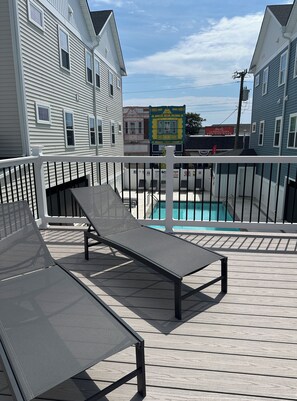 Une terrasse avec deux chaises longues, une piscine et une vue sur les bâtiments voisins.