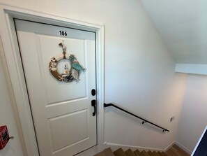 Une porte blanche portant le numéro 106, une guirlande décorée sur le thème de la marine, un détecteur d’incendie et un escalier en bois avec une rampe noire.
