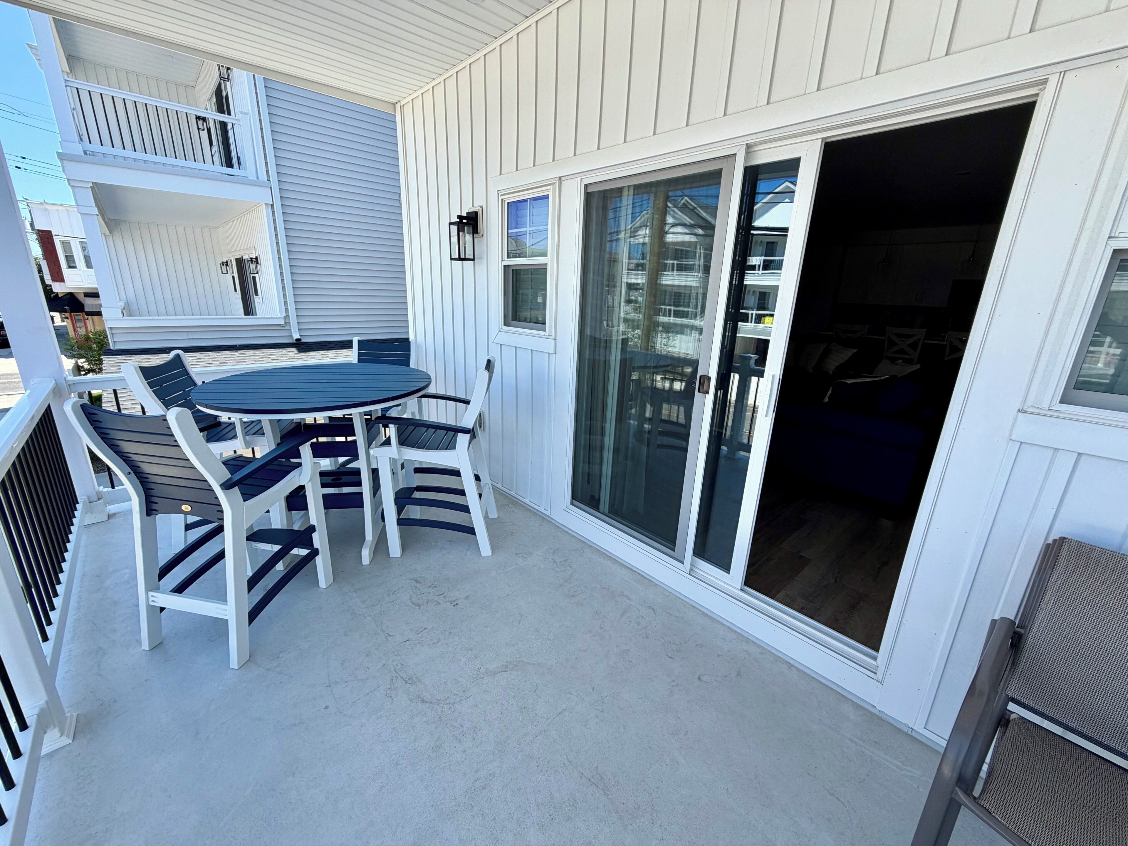 Une terrasse couverte avec une table ronde et des chaises, une porte-fenêtre coulissante et un mur extérieur blanc.
