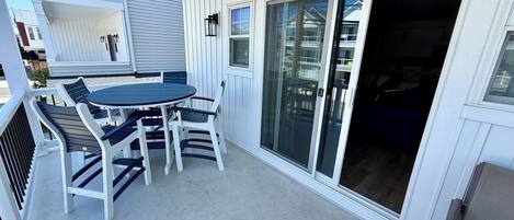 Une terrasse couverte avec une table ronde et des chaises, une porte-fenêtre coulissante et un mur extérieur blanc.