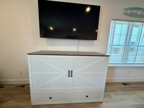 A white cabinet with drawers, a mounted television, and a window with blinds. - 158 E Garfield Ave  Unit 106 Wildwood, NJ (Wildwood)