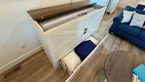 Una sala de estar moderna con una consola de madera empotrada, un mueble blanco con cajones, un sofá azul y un televisor montado en la pared.
