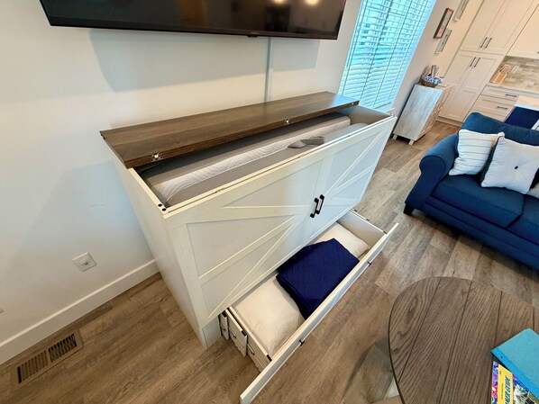 A modern living room with a built-in wooden console table, a white cabinet with drawers, a blue sofa, and a television mounted on the wall. - 158 E Garfield Ave  Unit 106 Wildwood, NJ (Wildwood)