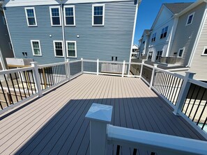 A wooden deck with white railings, a clear sky, and a blue building in the background. - 158 E Garfield Ave  Unit 106 Wildwood, NJ (Wildwood)