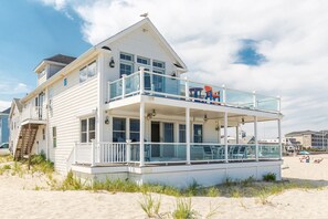 Ein zweistöckiges Strandhaus mit Balkon, überdachter Terrasse und Blick auf den Strand.