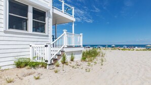 A beachfront property with a white exterior, a balcony, and a sandy beach in the background. - Hamptons Best Beach House. On the Sand. Sleeps 8. Parking. Porch. Beach Gear (Hampton)