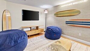 A modern living room with a flat-screen TV, wooden surfboards on the wall, and a bean bag chair. - Hamptons Best Beach House. On the Sand. Sleeps 8. Parking. Porch. Beach Gear (Hampton)