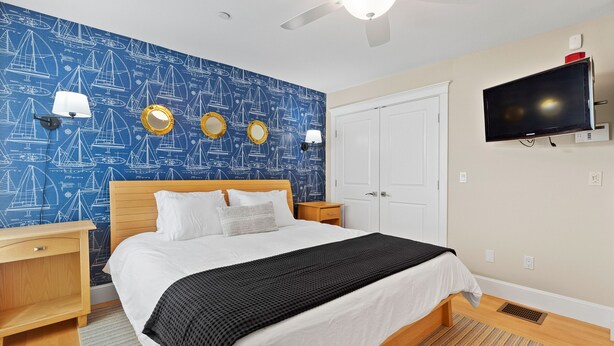 A hotel room with a bed, a TV, a ceiling fan, and a wall with nautical-themed wallpaper. - Hamptons Best Beach House. On the Sand. Sleeps 8. Parking. Porch. Beach Gear (Hampton)