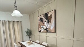 Comedor con mesa, sillas, lámpara colgante, un cuadro y una planta.