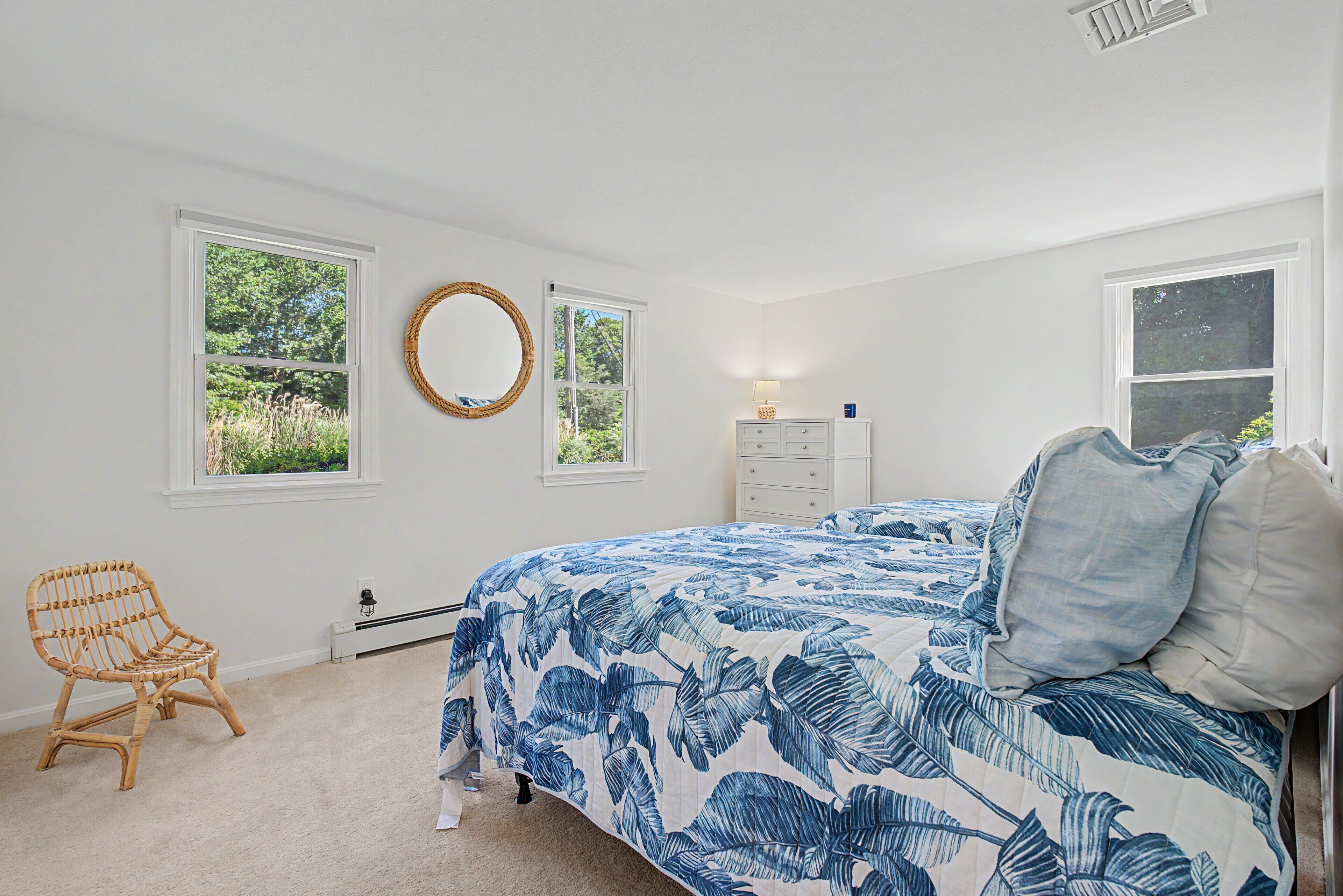 A bedroom with a bed, a chair, a dresser, and two windows.