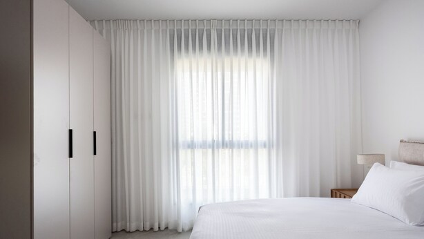 A hotel room with a large bed, a nightstand, a lamp, and a wardrobe. - Elegant 4BR Stay l Balcony & Mamad (Bat Yam)