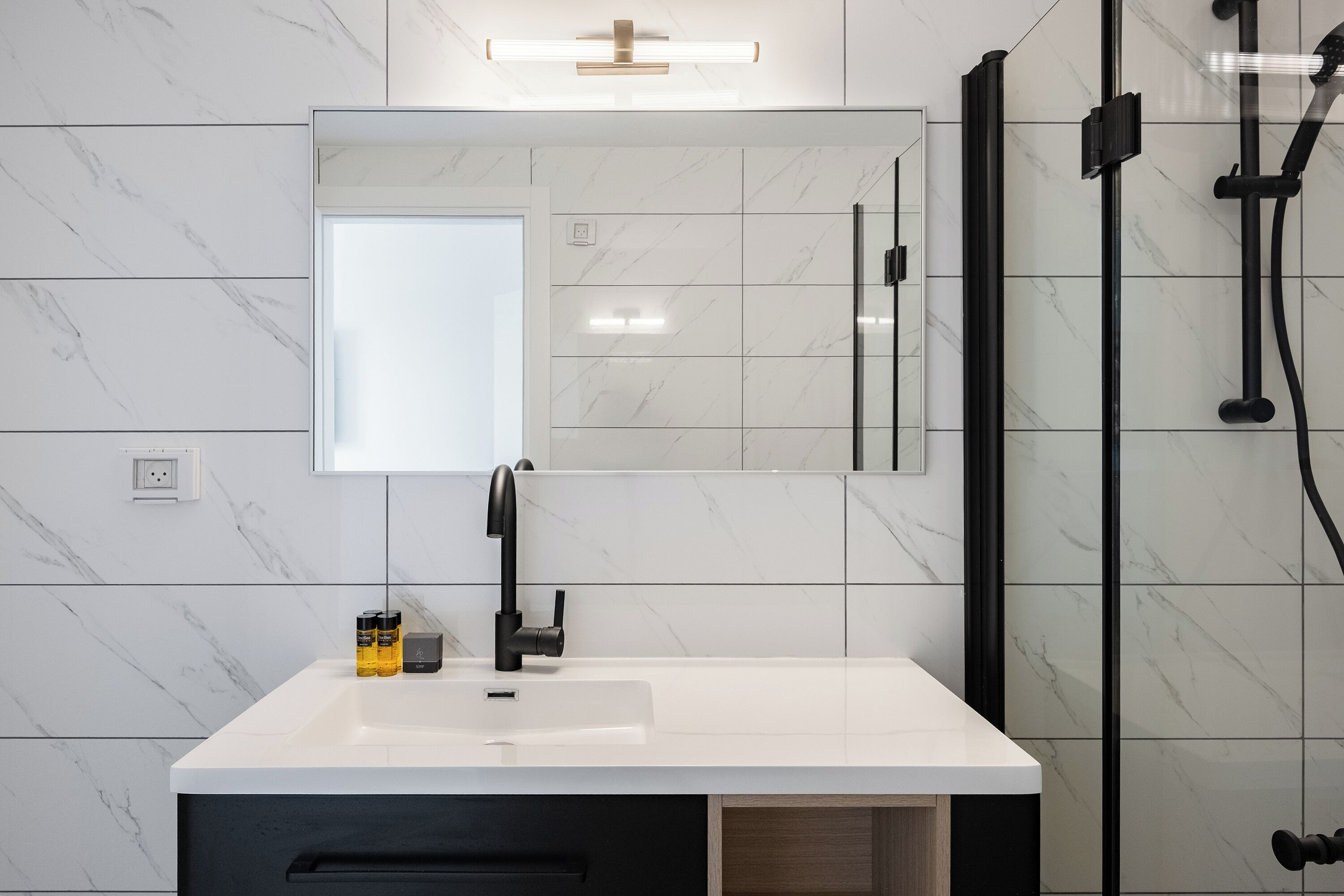 Un baño moderno con un lavamanos de mármol blanco, un grifo negro y una ducha con cerramiento de vidrio.