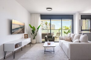 Ein modernes Wohnzimmer mit Sofa, Couchtisch, Fernseher und einem großen Fenster mit Blick auf Gebäude.