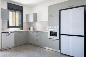 Eine moderne Küche mit grauen Schränken, einem Geschirrspüler, einem Backofen und einem Kühlschrank mit zwei Türen.