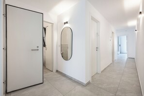 Ein moderner Flur mit weißen Wänden, einem großen Spiegel und einer Tür zu einem Badezimmer.