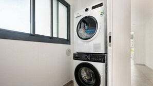 A laundry room with a front-loading washer and dryer, a window, and a tiled floor. - Elegant 4BR Stay l Balcony & Mamad (Bat Yam)