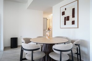 A dining area with a round table, six chairs, a vase with dried plants, and a framed abstract artwork on the wall. - Elegant 4BR Stay l Balcony & Mamad (Rishon LeTsiyon)