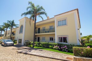 A multi-story building with balconies, a paved driveway, and a parked car. - Casa Coelha - Garden Apartment near the Coast (Albufeira)