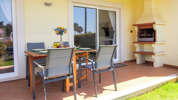 Eine Terrasse im Freien mit Tisch, Stühlen, einem Grill und einer Glasgleittür.