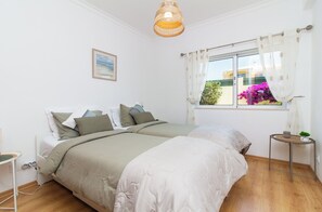 A bedroom with a bed, bedside table, and a window with curtains. - Casa Coelha - Garden Apartment near the Coast (Albufeira)