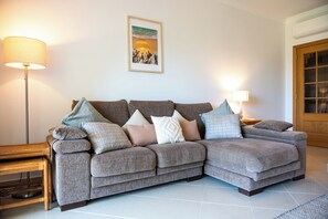 Ein modulares Sofa mit mehreren Kissen, eine Stehlampe, ein gerahmtes Bild an der Wand und eine Holztür.