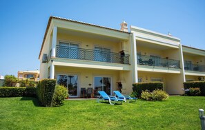 Ein zweistöckiges Gebäude mit Balkon, Rasen und Liegestühlen.