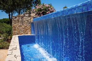 A swimming pool with a stone wall and a waterfall feature. - Casa Coelha - Garden Apartment near the Coast (Albufeira)