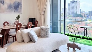 A modern living room with a curved sofa, dining area, and a view of a cityscape through large windows. - The Velvet Nook Rooftop Pool and Gym (Nairobi)