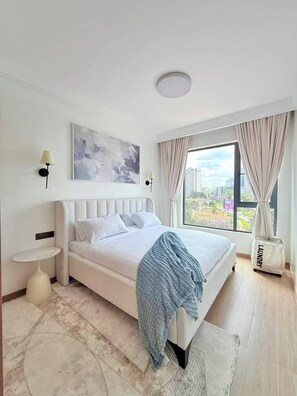 A modern bedroom with a large bed, a city view, a painting on the wall, and a laundry bag. - The Velvet Nook Rooftop Pool and Gym (Nairobi)