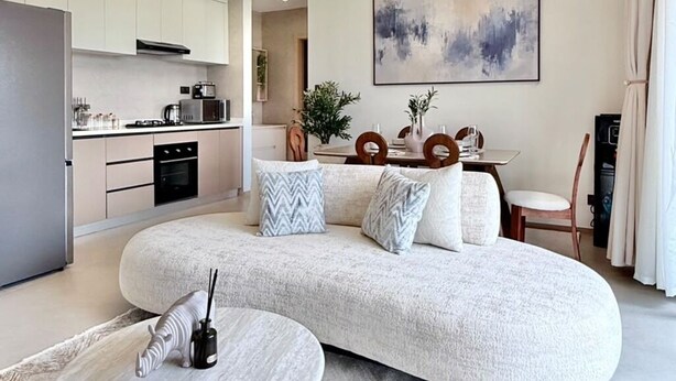 A modern living room with a large L-shaped sofa, a round coffee table, and a dining area with a table and chairs. - The Velvet Nook Rooftop Pool and Gym (Nairobi)
