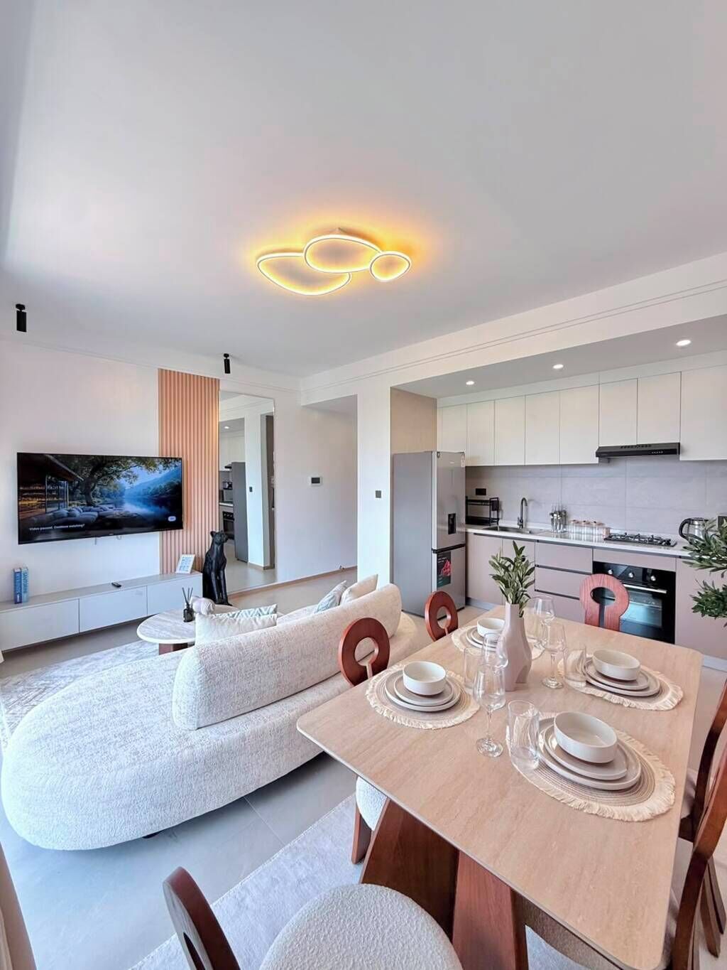 Ein modernes Wohnzimmer mit Flachbildfernseher, einer Couch und einer Essecke mit Tisch für vier Personen.