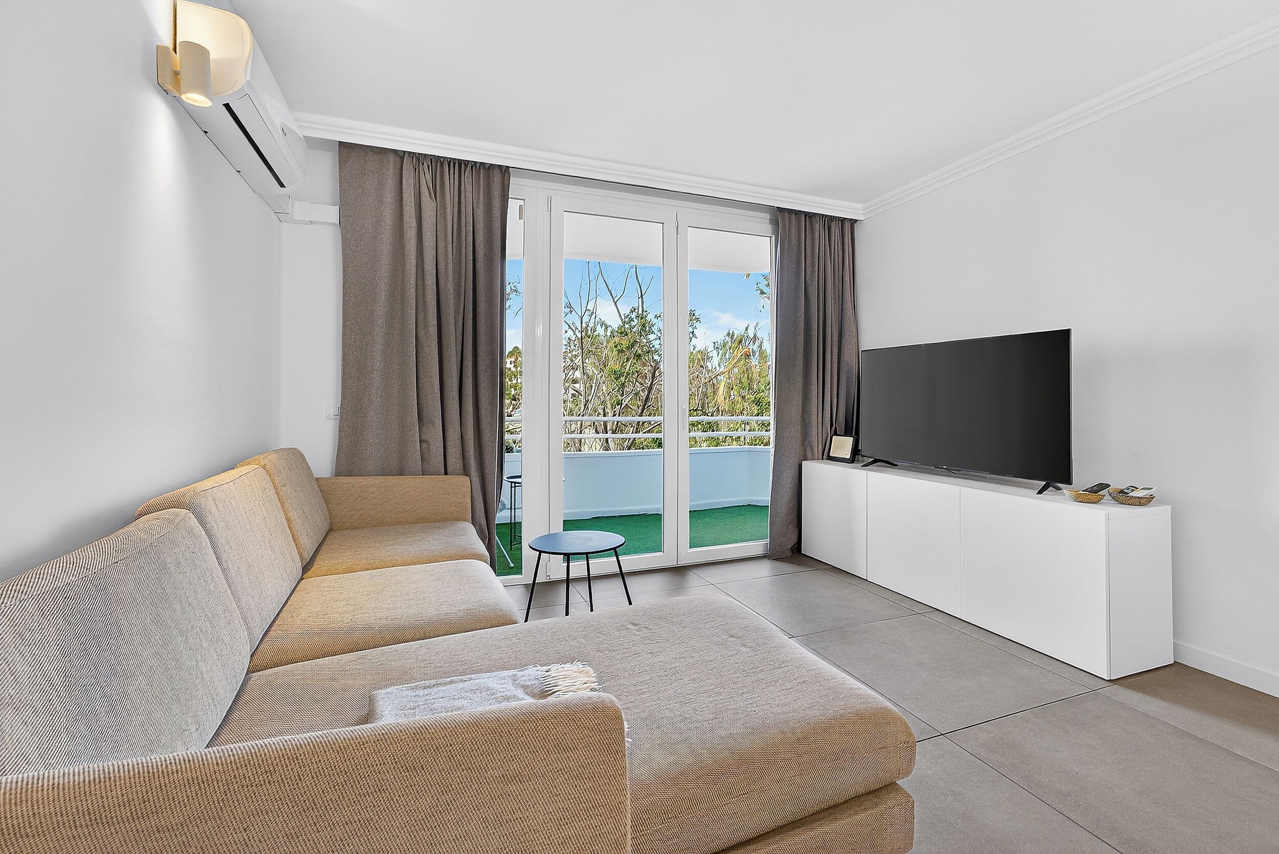 Ein modernes Wohnzimmer mit einer Couch, einem Flachbildfernseher und einer Schiebeglastür, die auf einen Balkon führt.