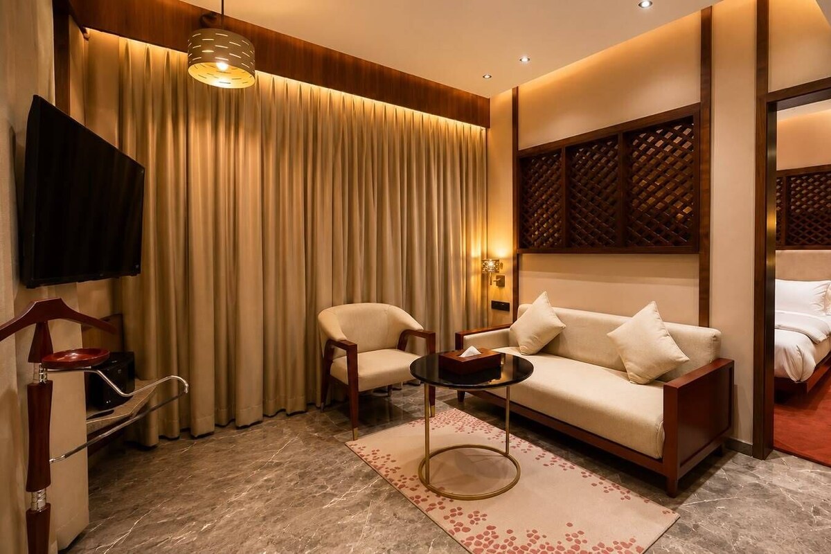 Une chambre d’hôtel avec un canapé, un fauteuil et une petite table. Un téléviseur est fixé au mur, et une porte donne accès à la salle de bain.