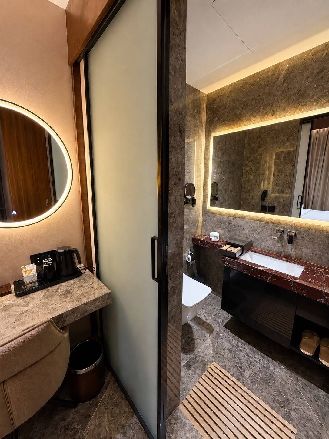 A modern bathroom with a marble vanity, a large mirror, and a separate toilet area.