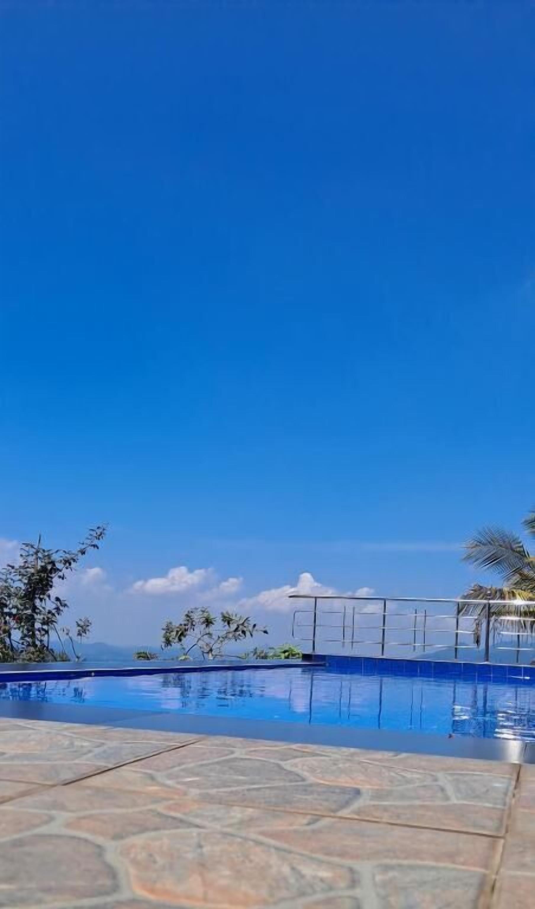A clear blue sky above a swimming pool with a stone-tiled deck.